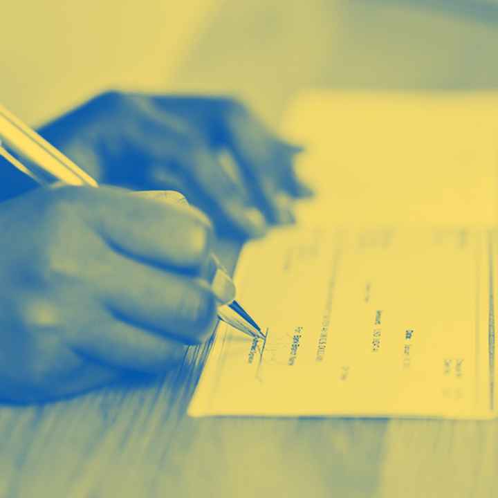 A yellow tinted image on someone signing a check on a desk.