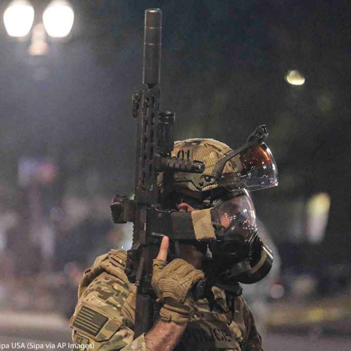 An ICE agent holds his weapon in the air as federal officers clear Main Street in Portland, Ore., on July 26, 2020.